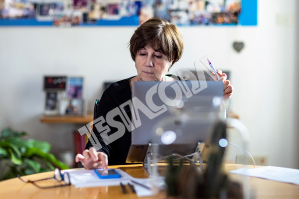 Aged lady Senior Consultant writes message on her mobile phon working remotely from home in a video meeting with her laptop on a round wooden table