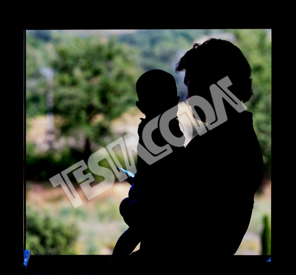 Backlight image of dad with his cute baby in his arms looking at smartphone at the window . In the blurred background green nature bushes and trees