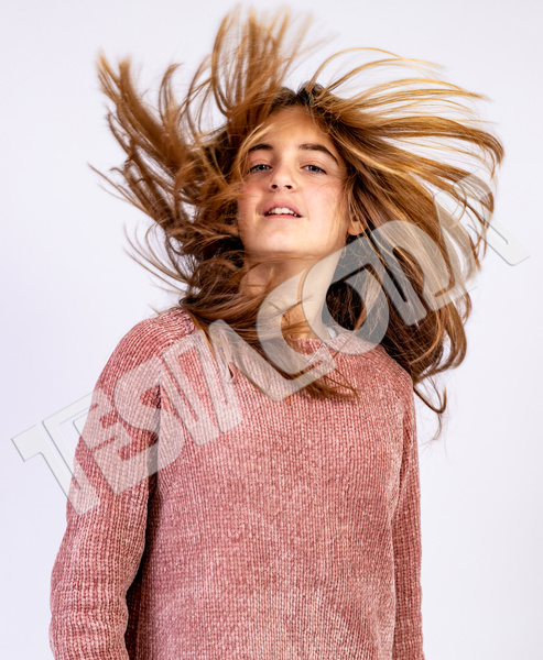 Young pretty smiling girl with blond long hair in pink t-shirt shaking her head with hair dishevelled by the wind in a glamorous pose