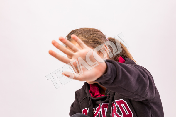 Young girl with sweatshirt hides her face and shields herself with her left hand blurred in the foreground not wanting to be photographed