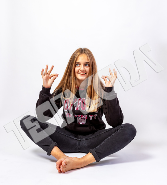 Smiling and bubbly cute blonde girl in playful oriental pose barefoot with funny and sly expression dressed casually with jeans and sweatshirt